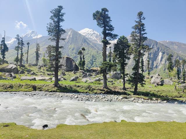 Green alpine meadows and snow-capped Himalayan peaks along the Har Ki Dun trek trail in spring