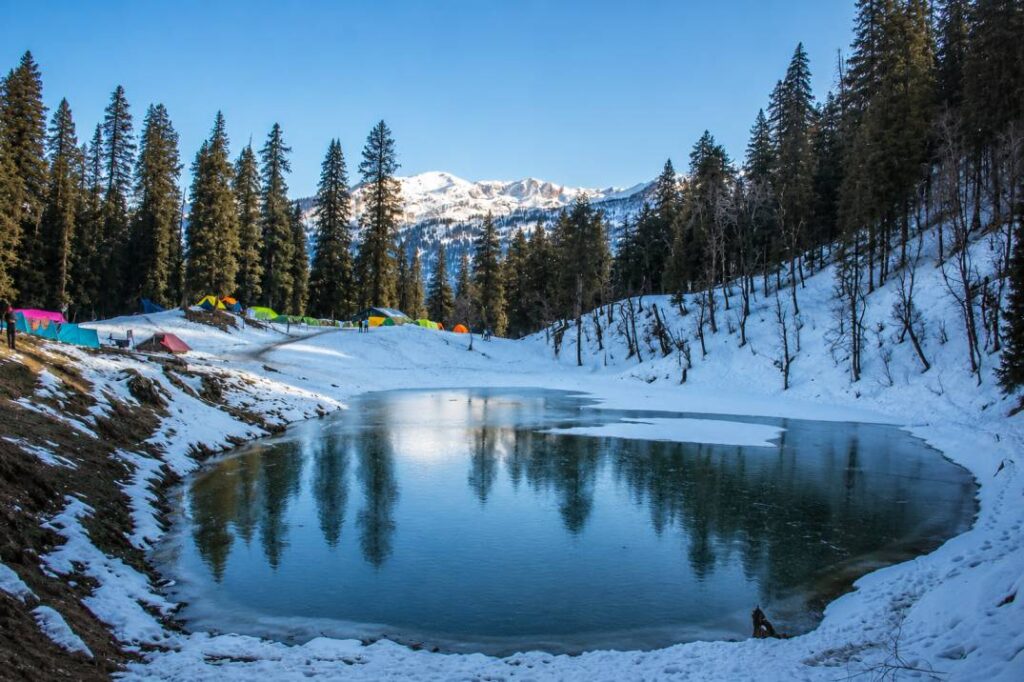 Scenic alpine lake Juda Ka Talab surrounded by dense pine forests on Kedarkantha trek route in Uttarakhand